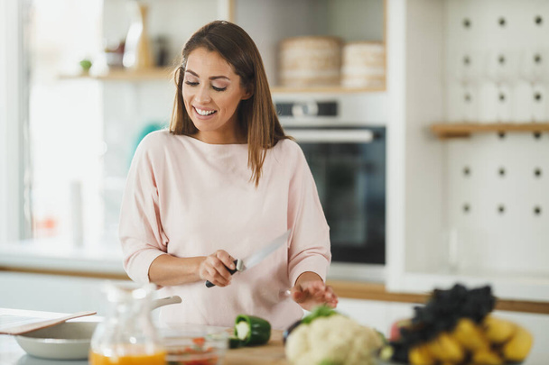 Aufnahme einer jungen Frau, die Gemüse hackt und in ihrer Küche eine gesunde Mahlzeit zubereitet. - Foto, Bild