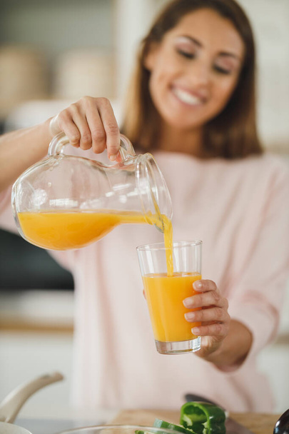 Tiro cortado de uma jovem mulher bebendo suco de laranja fresco em sua cozinha. - Foto, Imagem
