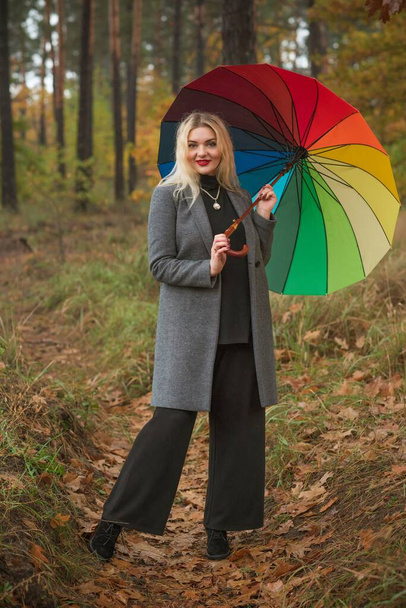 Mujer rubia agradable en el abrigo de otoño y paraguas colorido en el parque. Bastante más tamaño dama europea - Foto, imagen