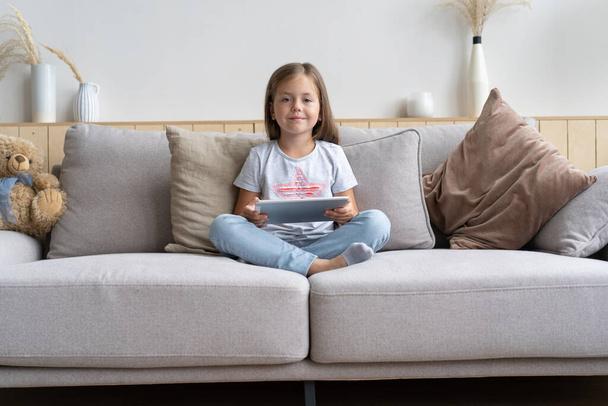 Little girl sitting on the sofa playing digital tablet in the living room at home. - Photo, image