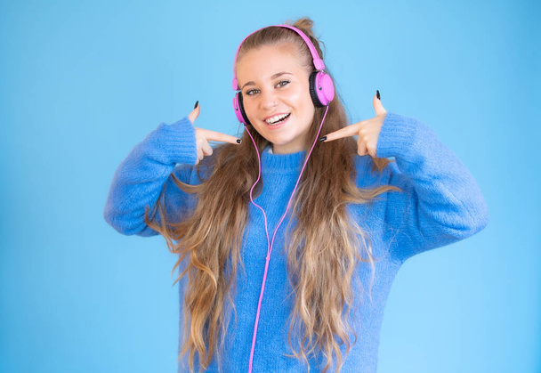 Krásná mladá žena ve sluchátkách poslech hudby ukazuje sama na modré pozadí - Fotografie, Obrázek