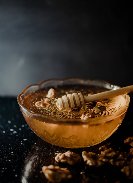 Wooden honey spoon dipped in a jar full of honey and nuts placed on a black background. Honey dripping around, pleasing and inviting photos. - Foto, afbeelding