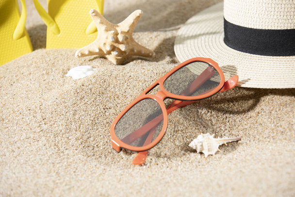 A pair of sunglasses, hat, slippers and a starfish on the sand on the beach - Foto, afbeelding