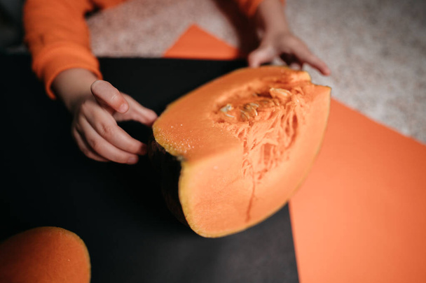 detailní fotografie chlapeckých rukou a plátek dýně na oranžovém a černém pozadí  - Fotografie, Obrázek