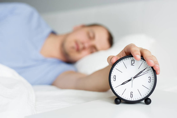 Концепция доброго утра - крупный план сонного человека, выключающего будильник на тумбочке - Фото, изображение