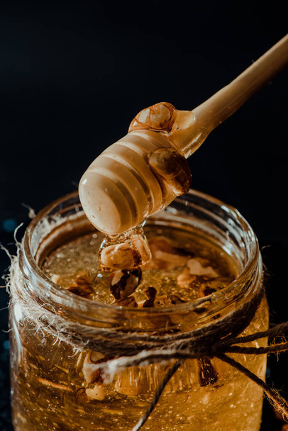 A vertical shot of honey in a glass jar with walnuts and wooden dipper - Фото, зображення