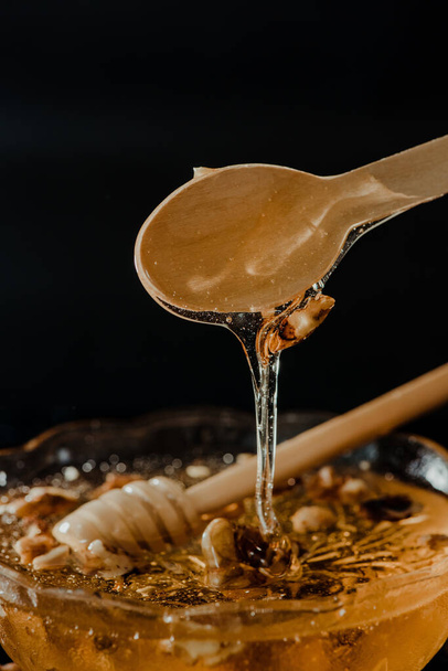 The honey in a glass bowl with wooden spoons in it dripping slowly and decorated with walnuts - Foto, Bild