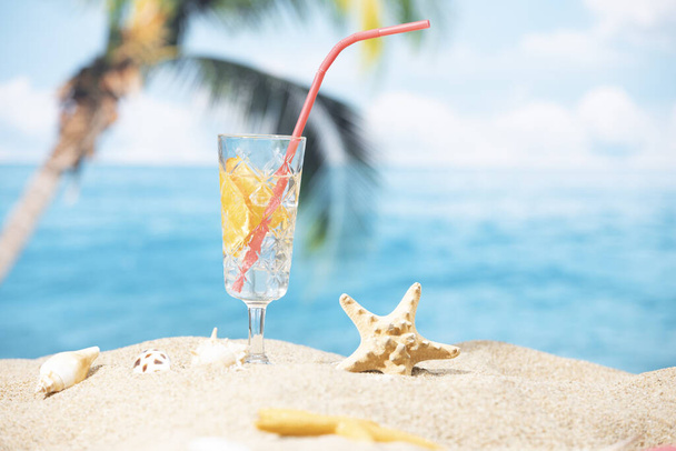A glass of lemon water placed on the sand on a palm tree and ocean background - Fotó, kép