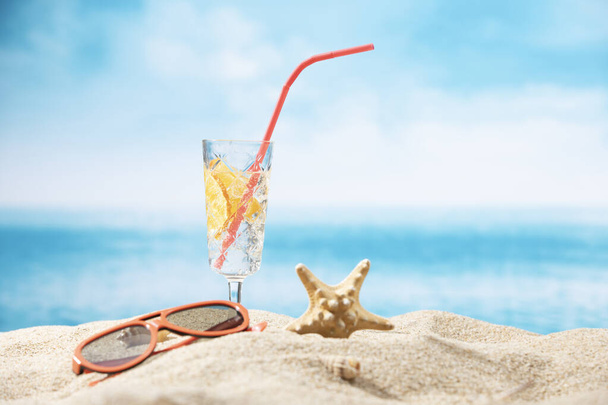 A starfish, sunglasses and a glass of lemon water on the sand on an ocean background - Fotó, kép