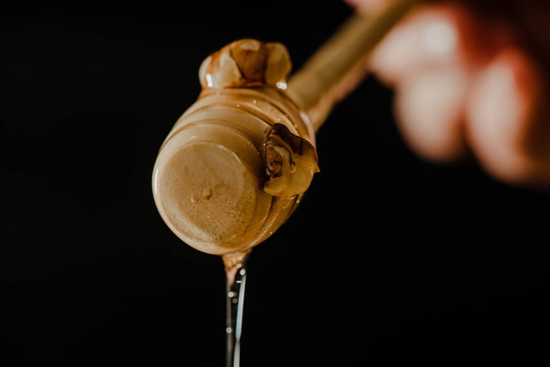Wooden honey spoon dipped in a jar full of honey and nuts placed on a black background. Honey dripping around, pleasing and inviting photos. - Fotografie, Obrázek