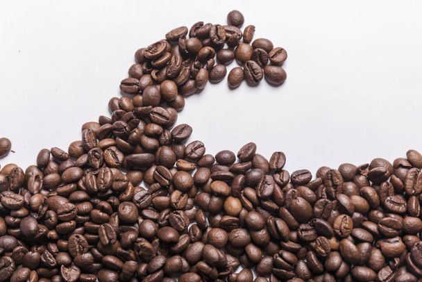 granos de café tostados de diferentes tonos de marrón dispersos en una superficie blanca en una ola. Fondo de café o concepto de textura. - Foto, imagen