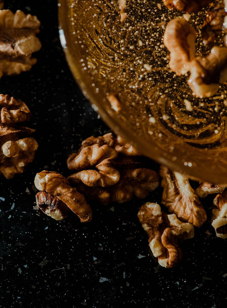 Wooden honey spoon dipped in a jar full of honey and nuts placed on a black background. Honey dripping around, pleasing and inviting photos. - Φωτογραφία, εικόνα