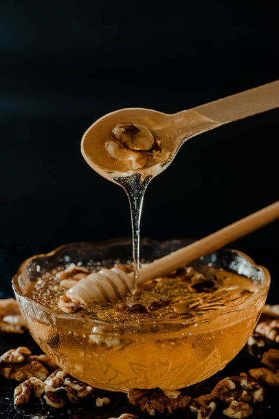The honey in a glass bowl with wooden spoons in it dripping slowly and decorated with walnuts - Foto, Bild