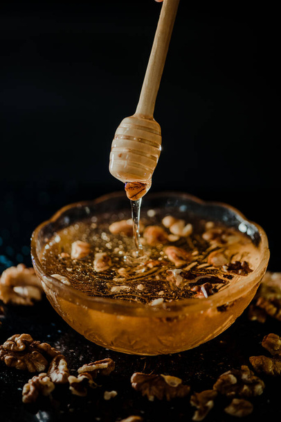 Wooden honey spoon dipped in a jar full of honey and nuts placed on a black background. Honey dripping around, pleasing and inviting photos. - Foto, Imagen