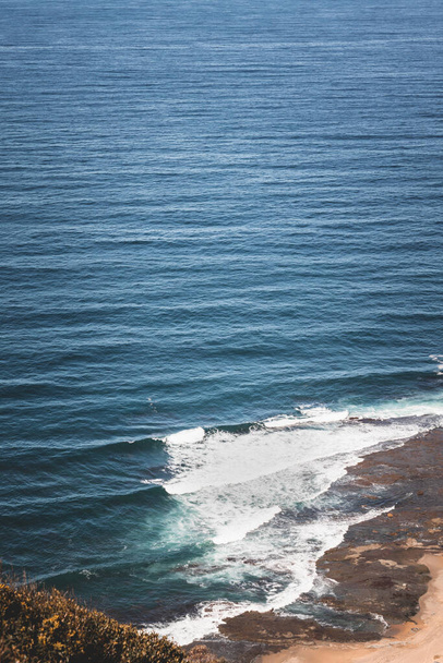 A high angle shot of the ocean as seen from a grassy cliff in the coast of New South Wales, Australia - 写真・画像