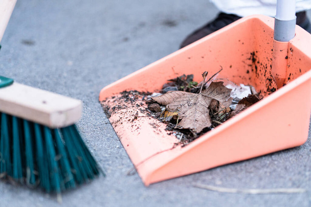 A closeup of a green street broom and dustpan used in cleaning a pavement - 写真・画像
