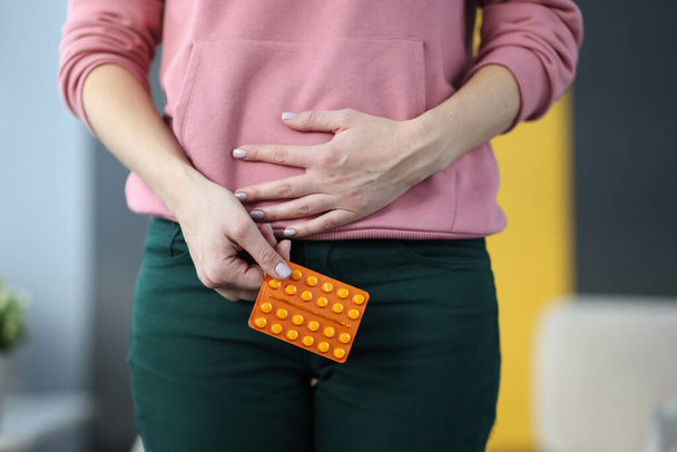 Женщина с таблетками в руках держит нижнюю часть живота дома крупным планом - Фото, изображение