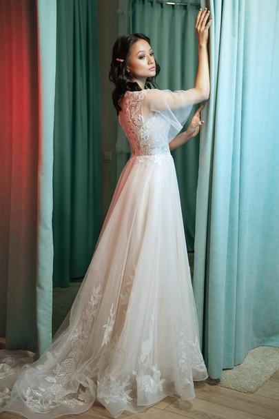 Портрет молодой невесты в модном свадебном платье с красивым макияжем и прической, студийное фото в помещении. Молодая, привлекательная модель азиатской внешности - Фото, изображение