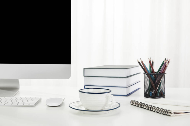 A closeup of a computer, a cup of coffee, books, and more on a white desk, indoors - Foto, Imagen