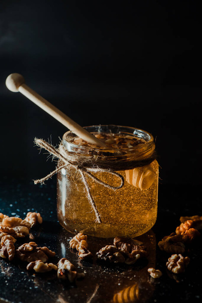 A vertical shot of honey in a glass jar with walnuts and wooden dipper - Фото, изображение