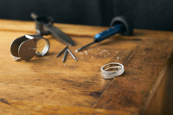 Workplace of a jeweler. Tools and equipment for jewelry work on an antique wooden desktop. Jeweller, engraver at work on jewelry made of diamonds and gold. Wood Platinum Diamond Metal Background - Photo, Image