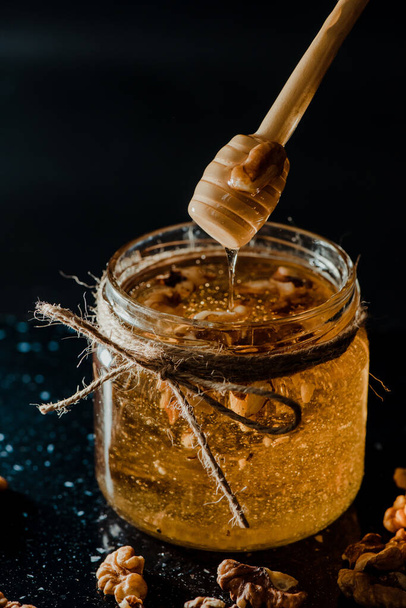 A vertical shot of honey in a glass jar with walnuts and wooden dipper - Valokuva, kuva