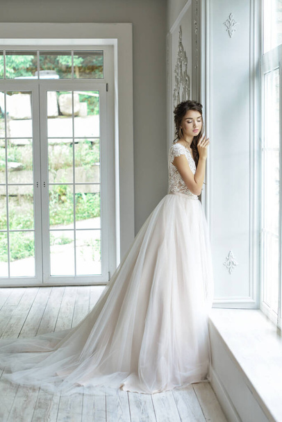 Портрет молодой невесты в модном свадебном платье с красивым макияжем и прической, студийное фото в помещении. Молодая, привлекательная модель - Фото, изображение