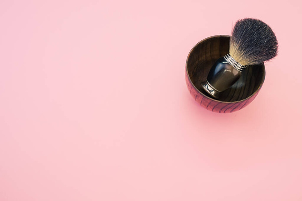 A high angle shot of a wooden shaving water bowl  near a shaving brush isolated on a pink background - Fotoğraf, Görsel