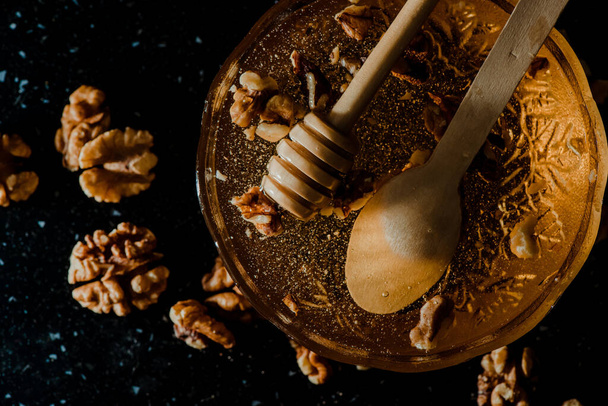 The honey in a glass bowl with walnuts and wooden spoons - Fotografie, Obrázek