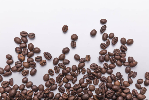 roasted coffee beans of various shades of brown scattered on a white surface with room for text. Coffee background or texture concept. - Foto, imagen