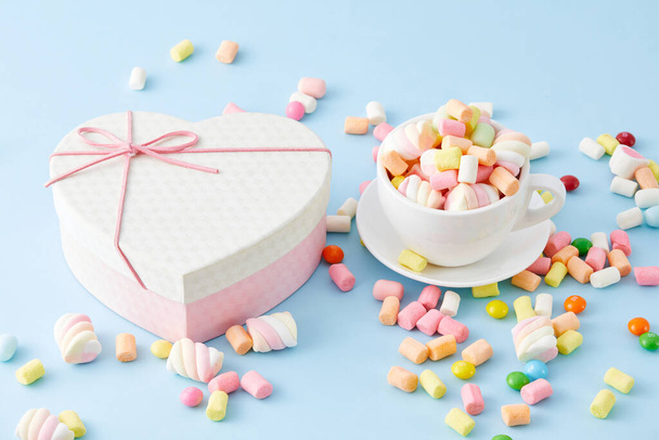 A closeup of a cup filled with marshmallows and a heart-shaped box isolated on a blue background - Foto, afbeelding