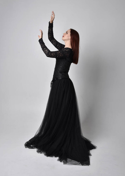 pełnowymiarowy portret kobiety ubranej w czarną gotycką sukienkę, stojącej na tle studia. - Zdjęcie, obraz