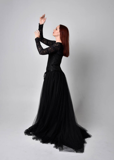 full length portrait of  woman wearing black gothic dress,  Standing pose  against a studio background. - Photo, Image