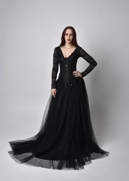 full length portrait of  woman wearing black gothic dress,  Standing pose  against a studio background. - Foto, afbeelding