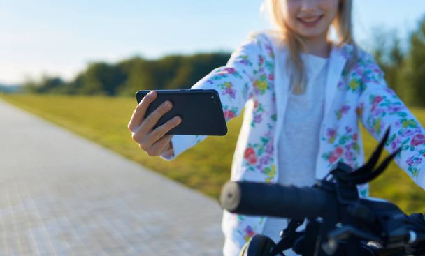 Young girl on a bicycle makes selfie on the phone - Фото, зображення
