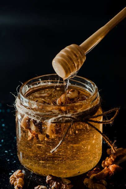 A vertical shot of honey in a glass jar with walnuts and wooden dipper - Valokuva, kuva