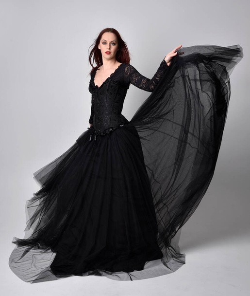 volledige lengte portret van vrouw dragen zwarte gotische jurk, Stand pose tegen een studio achtergrond. - Foto, afbeelding