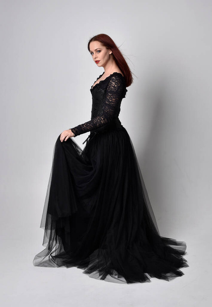 full length portrait of  woman wearing black gothic dress,  Standing pose  against a studio background. - Photo, image