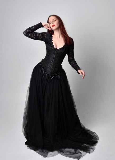 full length portrait of  woman wearing black gothic dress,  Standing pose  against a studio background. - Zdjęcie, obraz