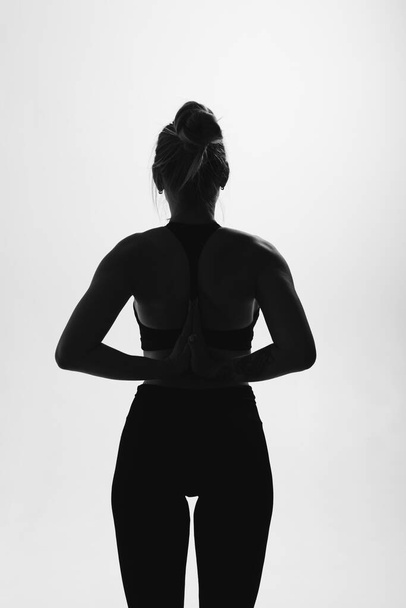 silhouet van blonde vrouw in zwart bodysuit staat met haar handen gevouwen achter haar rug - Foto, afbeelding