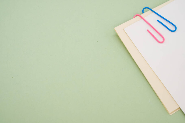 A closeup shot of a blank paper with colorful paper clips on a green background - Фото, изображение