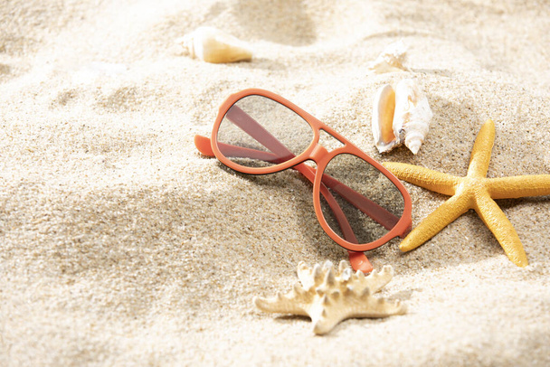A pair of red sunglasses and a starfish placed on the sand near the water - Foto, Imagem