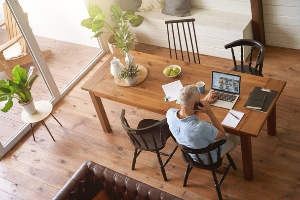 Вид зверху на зрілого кавказького бізнесмена, який сидить за столом у своїй сучасній квартирі і працює онлайн на ноутбуці
 - Фото, зображення