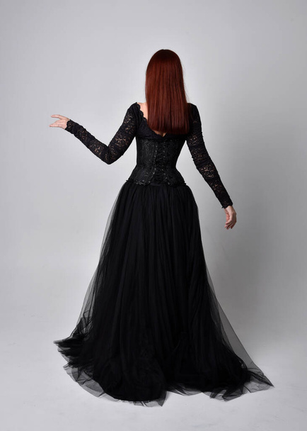 full length portrait of  woman wearing black gothic dress,  Standing pose with back to the camera against a studio background. - Foto, Imagem