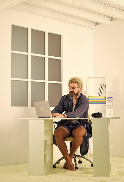 Online üzlet. Hipsteres férfi borotválatlan hajjal, laptoppal. A magányból hiányzik az emberi kölcsönhatás. Online videokonferencia. Egy fickó fürdőköpenyben otthon pihen. Távoli munka. Online kommunikáció - Fotó, kép