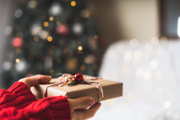 Öko-Weihnachtsgeschenk in Frauenhand. Glühender Schnee Bokeh, Tanne. Winterurlaub auf weißem Hintergrund. Null Abfall, plastikfrei - Foto, Bild