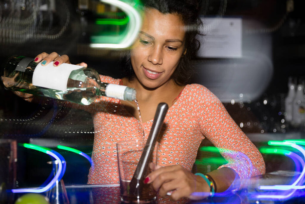 Retrato de una joven camarera que sirve una bebida alcohólica en el bar de una discoteca. Desenfoque de movimiento. - Foto, Imagen