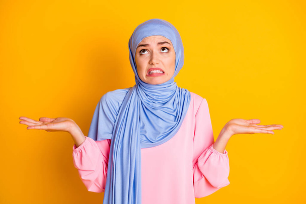 Portrait of attractive moody displeased desperate muslimah wearing hijab looking up isolated on bright yellow color background - Photo, image