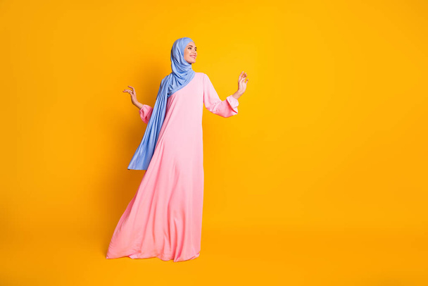 Full length body size view of nice fashionable cheerful feminine muslimah walking copy space isolated on vivid yellow color background - 写真・画像