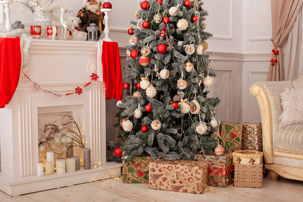 Decorated Christmas tree with gifts, fireplace and candles. Christmas tree decorated with toys and lights glowing garlands in living room. Xmas decoration concept. Cozy xmas interior room with sofa - Zdjęcie, obraz